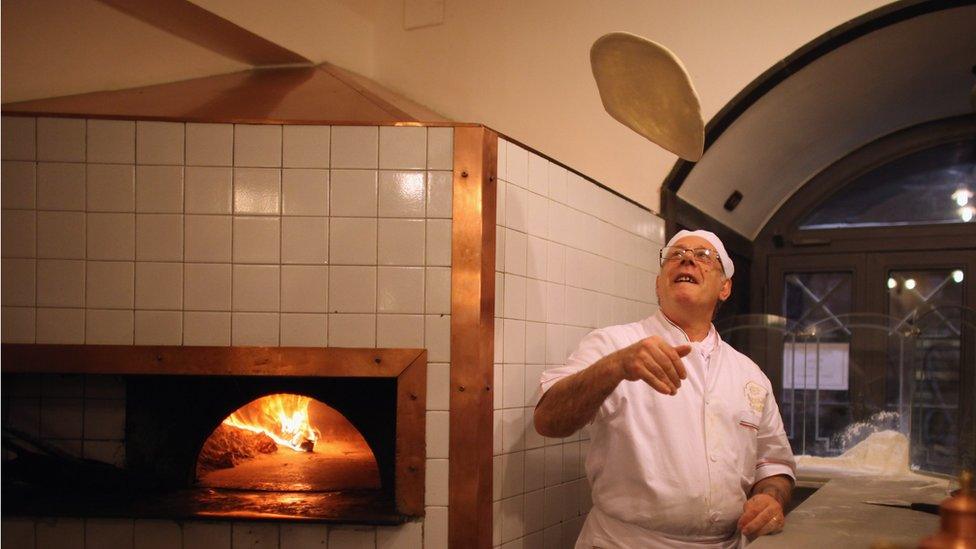 An Italian chef tosses a pizza base in the air in his restaurant kitchen