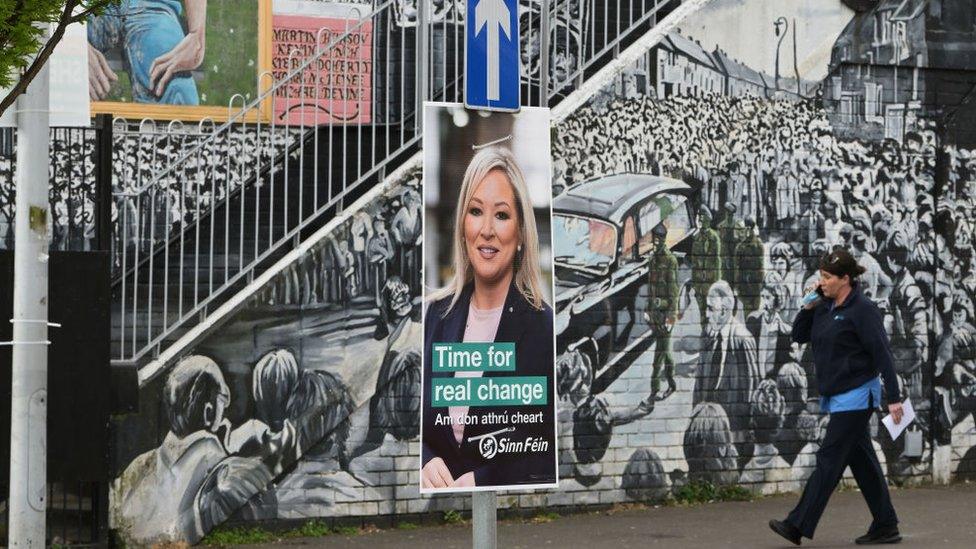 Sinn Féin's Michelle O'Neill election poster is seen against the backdrop of a republican mural in the nationalist area of west Belfast