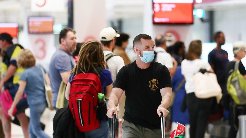 Traveller arriving from Melbourne wears a mask as he wheels baggage through crowd at Sydney domestic airport on 2 July 2020