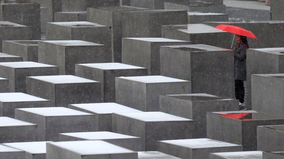 Woman stands with red umbrella at Berlin Holocaust memorial