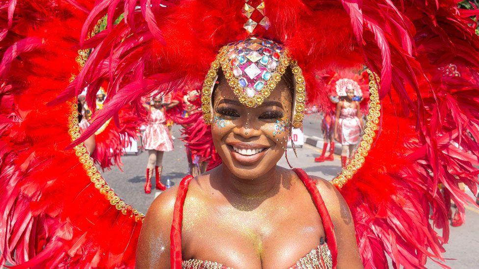 A woman taking part in Calabar's carnival smiles as she wears a massive red feathered headdress