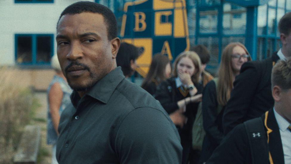 Ashley Walters with schoolchildren walking past him in a school yard in Adolescence