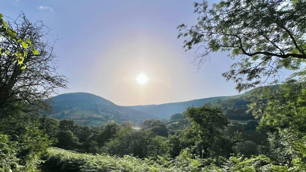 A landscape scene with the sun seen in the sky 