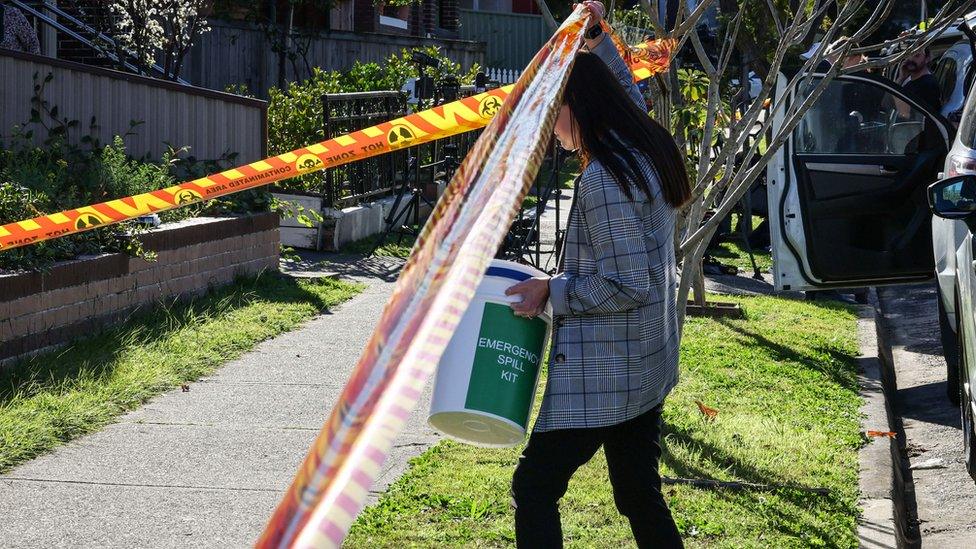 Woman walks under a cordon outside a home in Sydney where nuclear isotopes were found inside