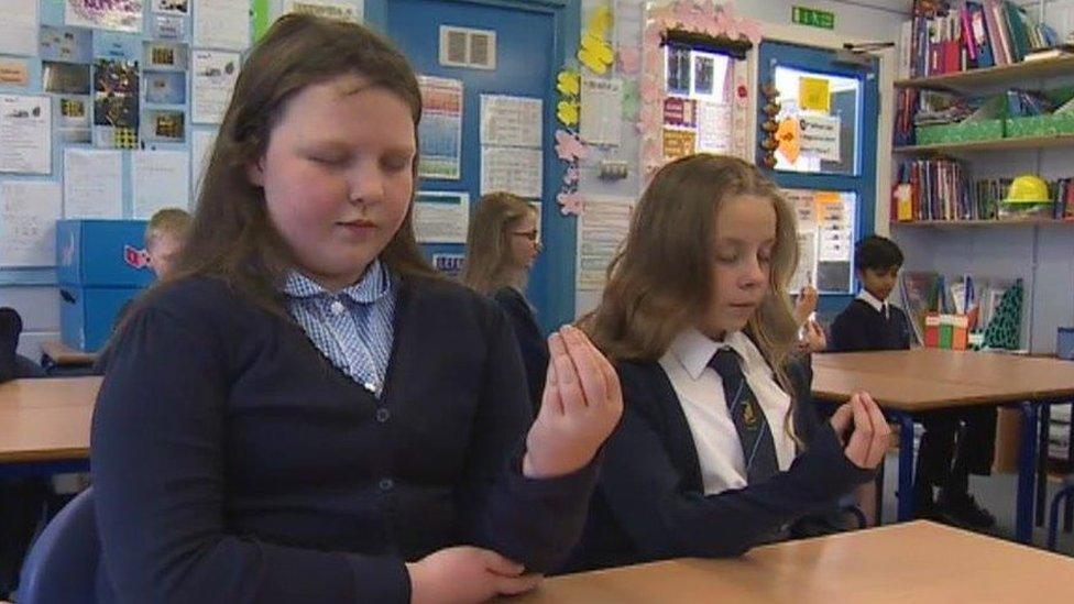 Two 10 year old girls holding a closed hand in the air with their eyes closed