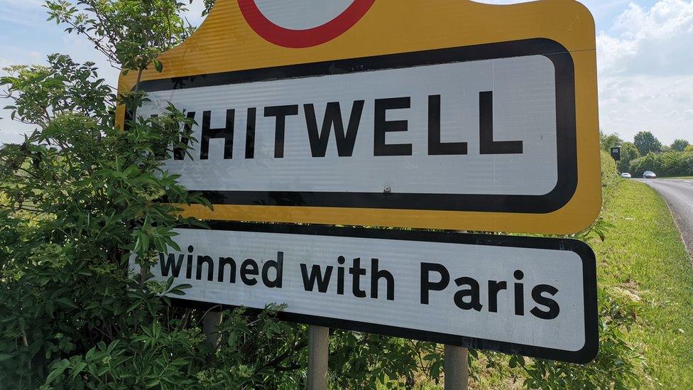 A road sign with a "twinned with Paris" sign