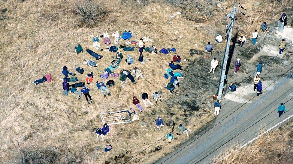 Members of Aum Shinrikyo cult wait outside during the raid on the headquarters