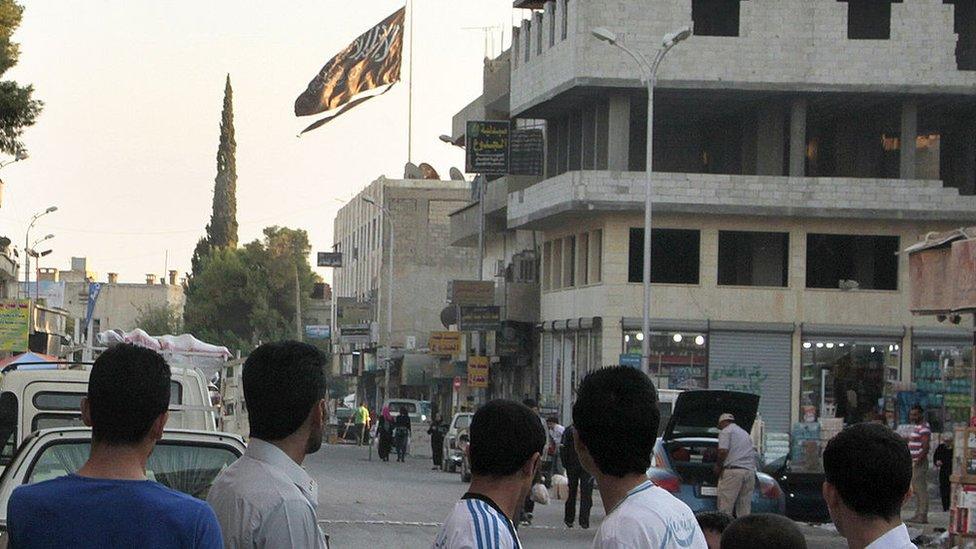 A group of men look at a large black jihadist flag with Islamic writing on it proclaiming in Arabic that "There is no God but God and Mohammed is the prophet of God" in the Syrian city of Raqqa (28 September 2013)