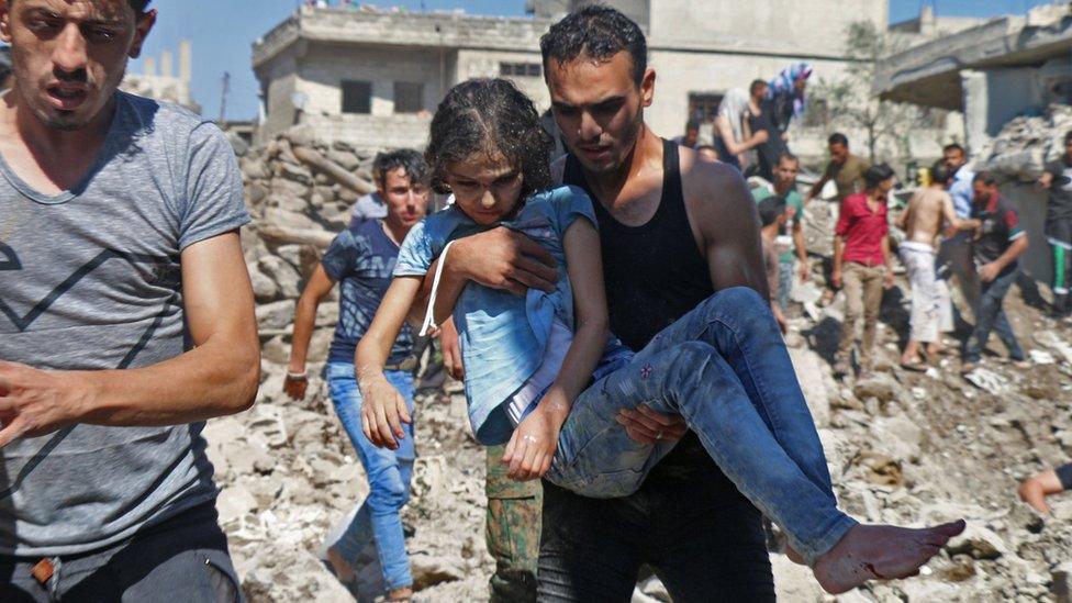 A man carries a girl rescued from a building hit in a suspected government air strike in the rebel-held town of Nawa, north of Deraa, Syria (26 June 2018)