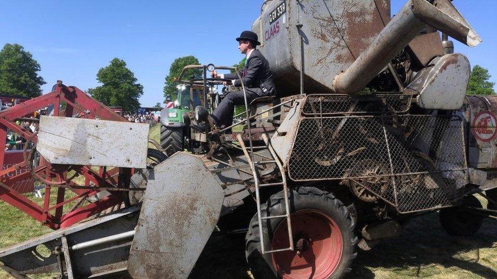 Man riding combine harvester in a suit and bowler hat