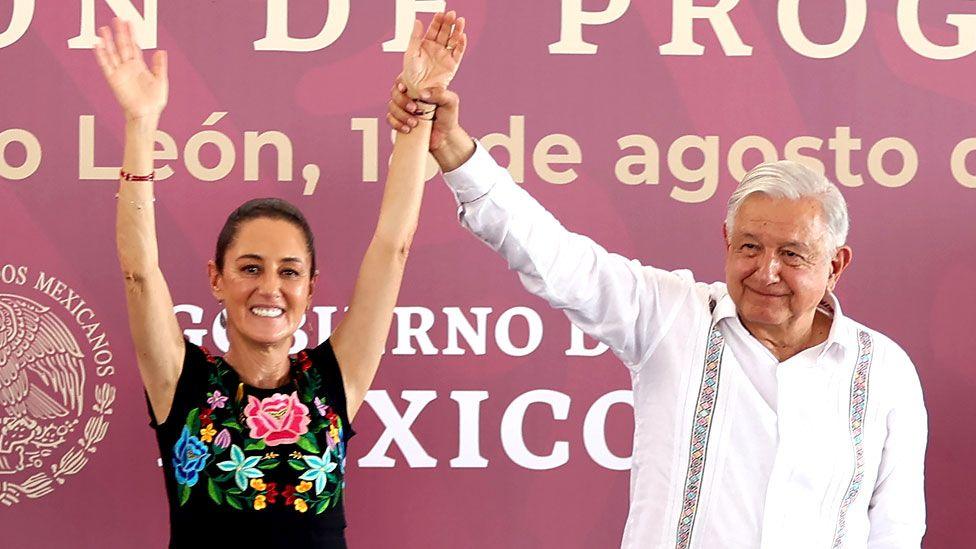 Andrés Manuel López Obrador holding up Claudia Sheinbaum's arms at an event back in August