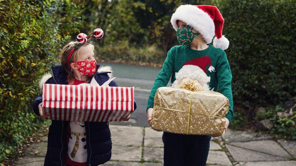 Two children giving Christmas presents while wearing face masks.