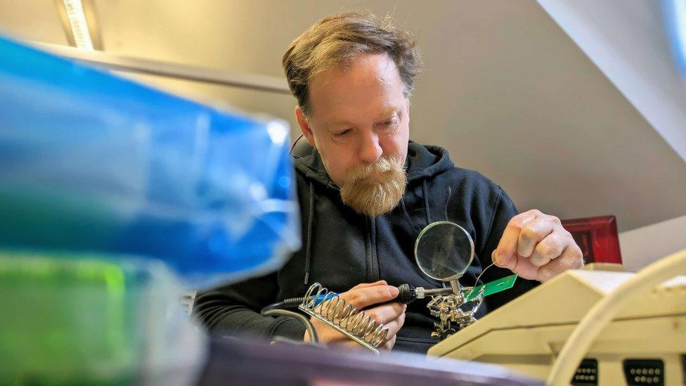 A man with a beard uses a soldering iron to fix a circuit board