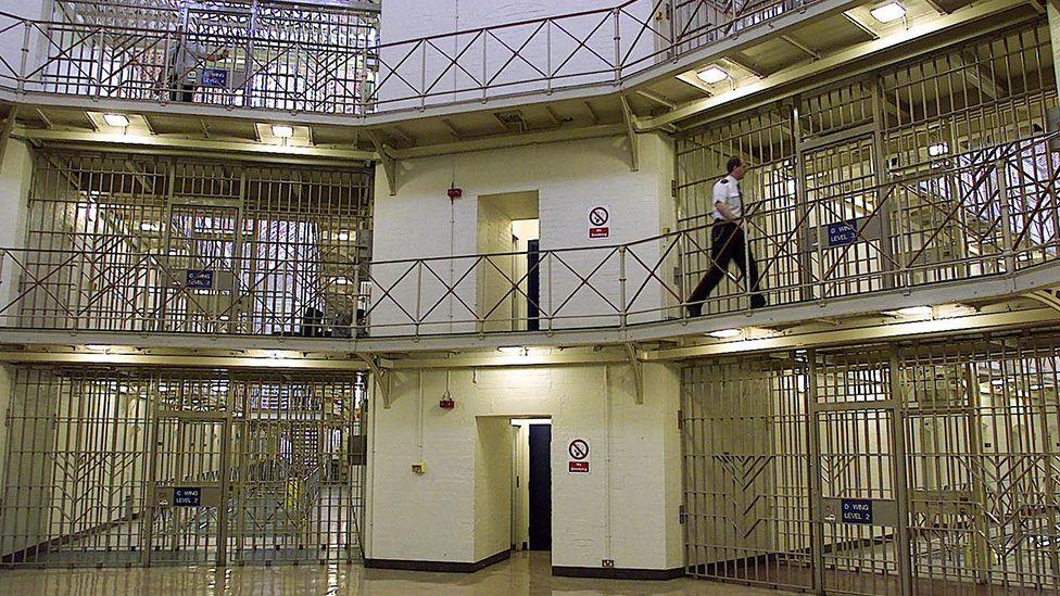 A prison officer walking in a rotunda area of an empty-looking prison on three levels with many iron gates and bars