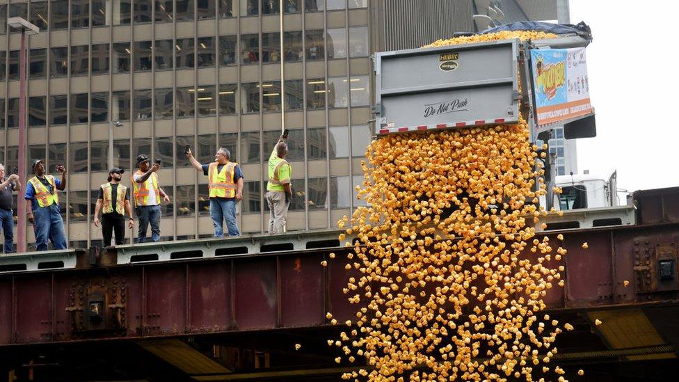 photograph shows a lorry emptying thousands of rubber ducks from a bridge with people watching nearby