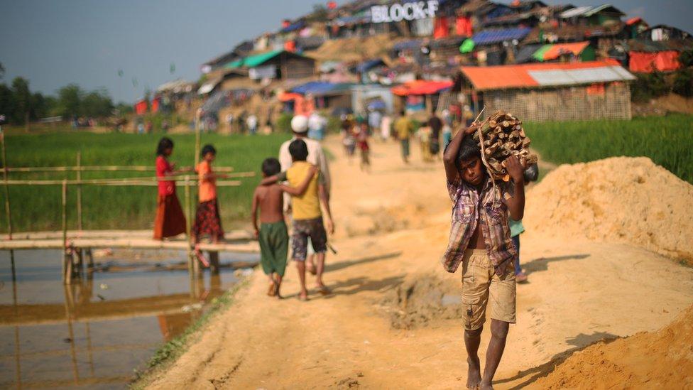 A young Rohingya boy carries a bundle of wood on his shoulder down the earthen path of Palong Khali refugee camp, Bangladesh