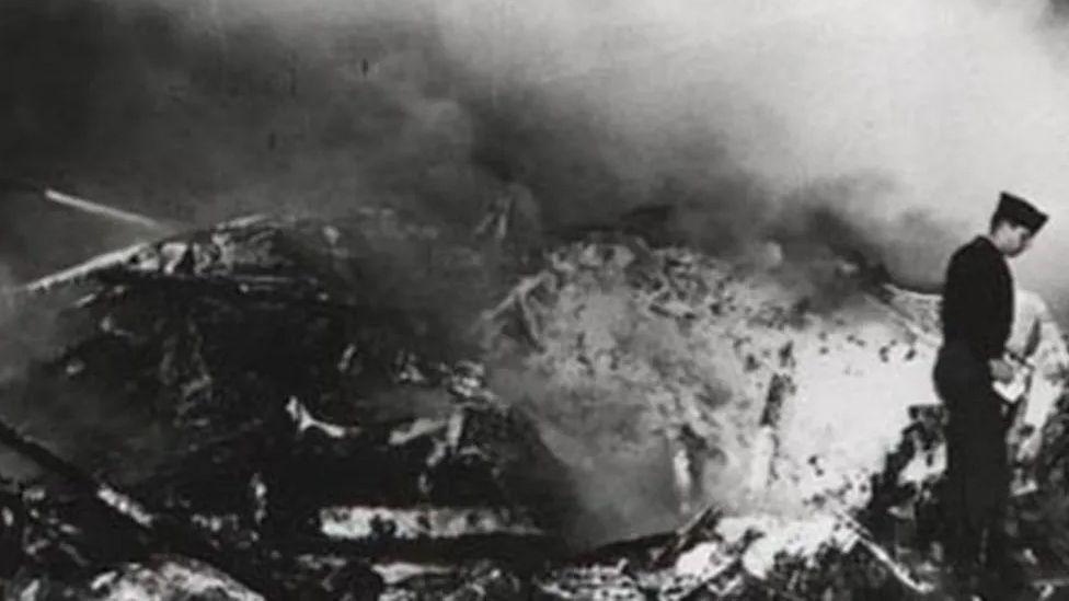 Black and white image of the plane wreckage with a soldier to the right