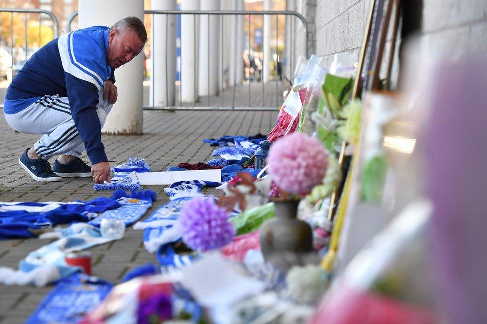 A man adds a Leicester City scarf to floral tributes lined up outside Leicester City Football Club's King Power Stadium in Leicester, eastern England, on October 28, 2018 after a helicopter belonging to the club's Thai chairman Vichai Srivaddhanaprabha crashed outside the stadium the night before