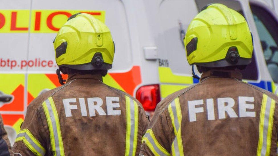 File image of two anonymous firefighters in brown uniform and yellow helmets outside the scene of a fire