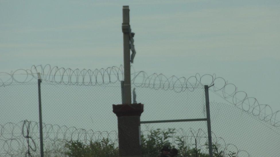 A statue of Christ on the crucifix visible from the Hungarian side of the border, above the razor wire