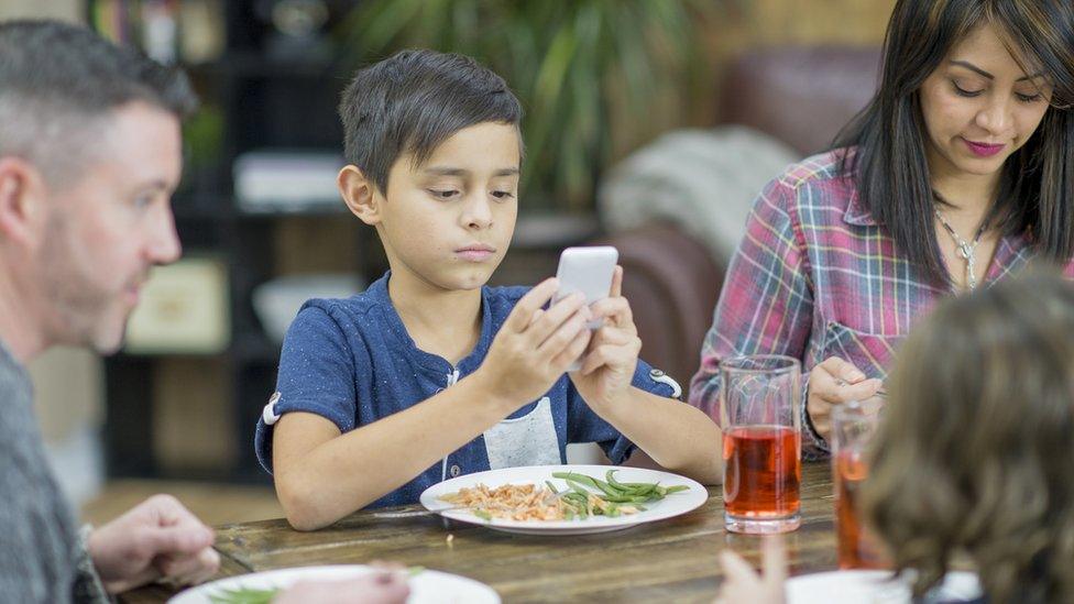 Child using phone at dinner table