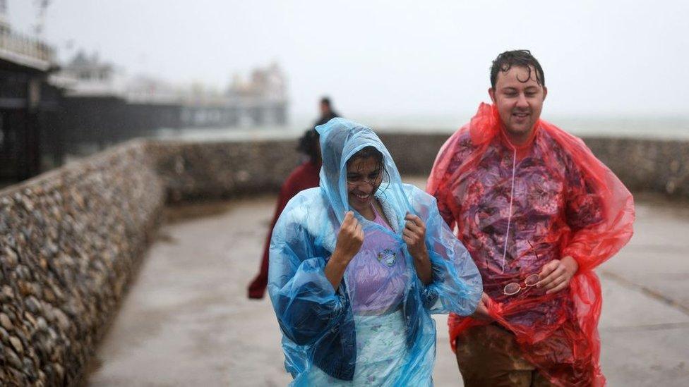 People walk in the rain in plastic ponchos in Brighton