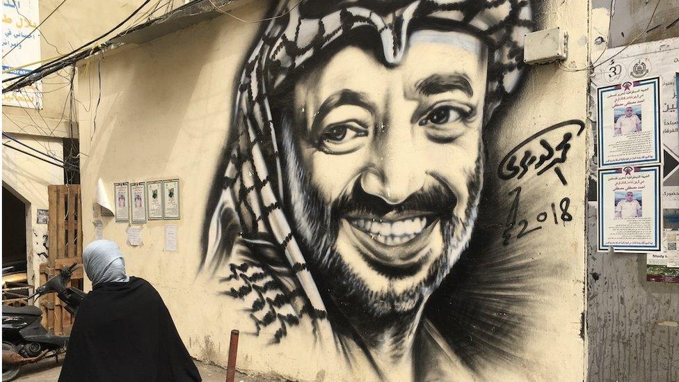 Woman walks past mural of Yasser Arafat in Bourj el-Barajneh refugee camp (Oct 2018)