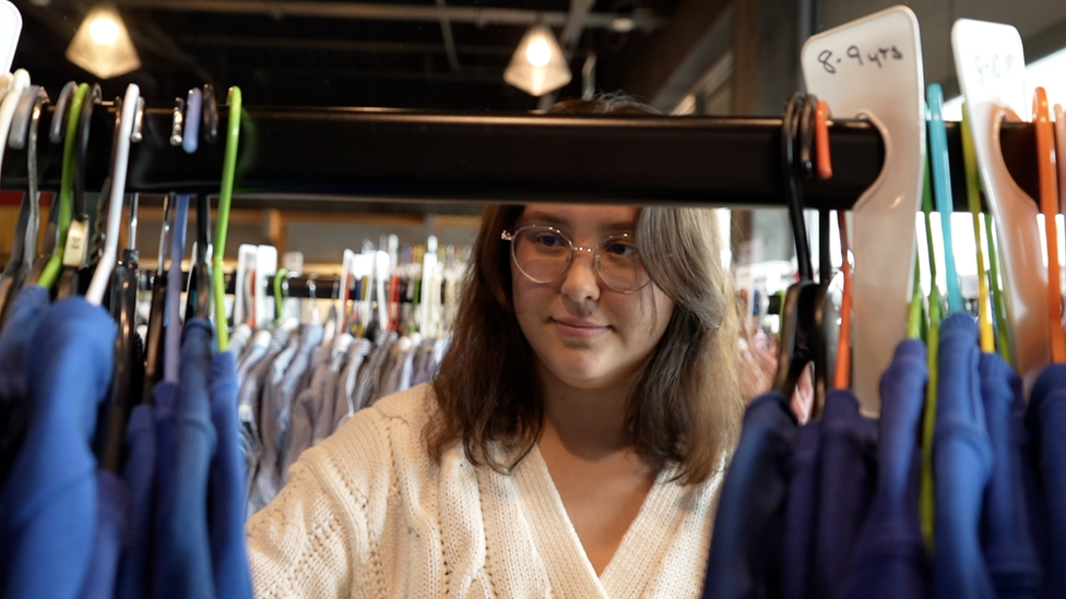 A woman browsing through hangers at the uniform exchange.