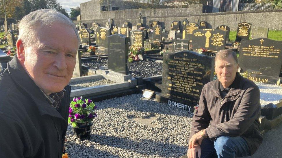 Two men kneel beside the grave of their brother in a cemetery