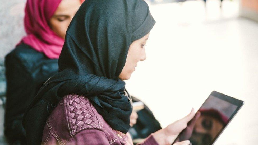 Women wearing headscarves look at a tablet computer