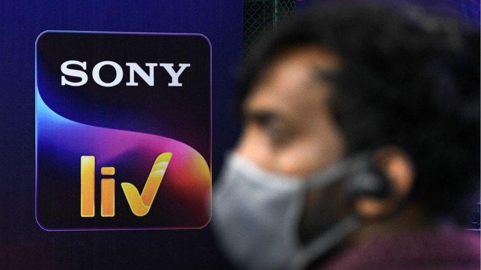 A man wearing a face mask is seen standing in front of a banner with a Sony liv logo in Mumbai.