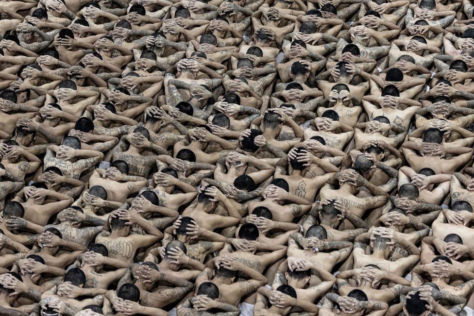 Prisoners with their hands over their heads and their faces turned away as they are transferred to the mega-jail Cecot in El Salvador