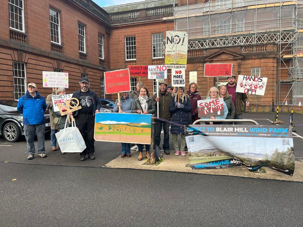 A group of wind farm protesters with placards stands outside Dumfries and Galloway Council HQ