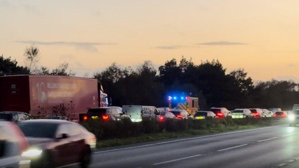 Blurred cars passing from the right to left.  Two lanes of traffic queueing with brakes lights on and ambulance with blue lights on moving through on the far left