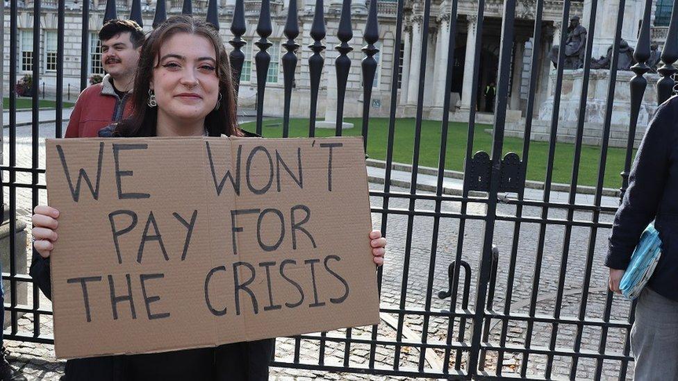 Hannah Pryor holds a sign that reads: We won't pay for the crisis