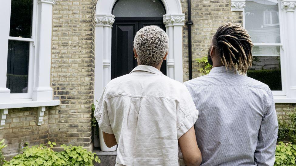 A couple stand in front of a house