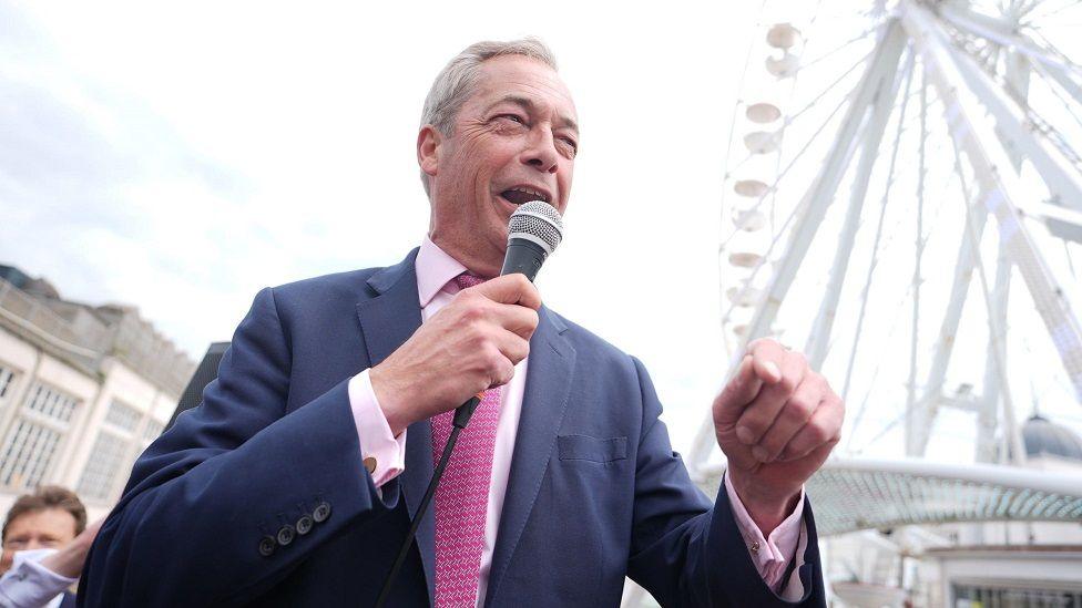 Nigel Farage addresses crowds in Clacton, with microphone in hand and ferris wheel in the background