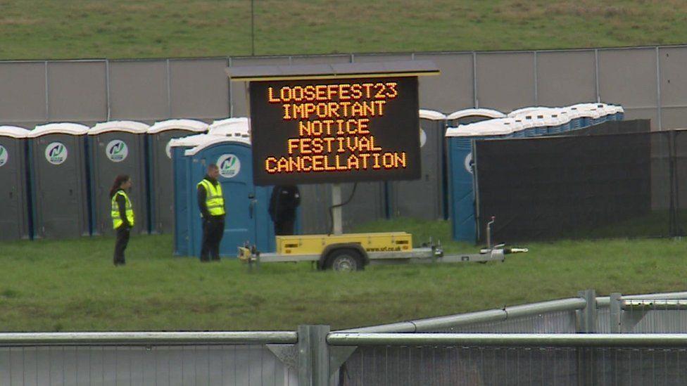 Electronic sign announcing LooseFest 2023 cancellation in front of rows of portable toilets.