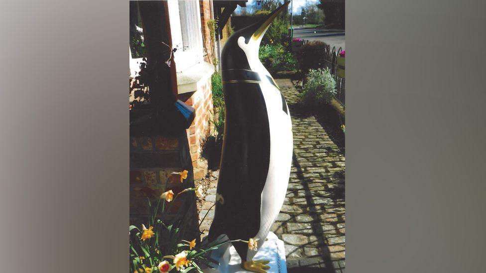 A four foot-high penguin decoration on a plinth in the front garden of a house.