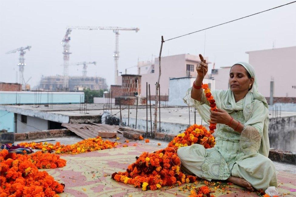 Shakila Bano, 38 years old, makes a garland of Marigold flowers at her house as the construction site of Hindu Ram Temple is seen in the background, in Ayodhya, India, November 22, 2023. REUTERS/Anushree Fadnavis