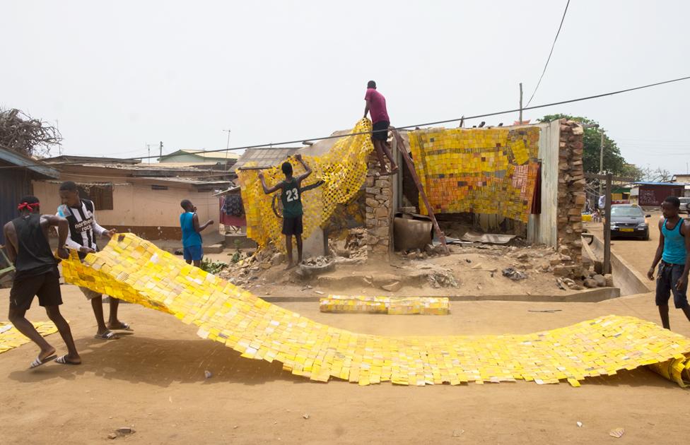 People spreading out yellow tapestry created by artist Serge Attukwei Clottey on a road in La - Accra, Ghana