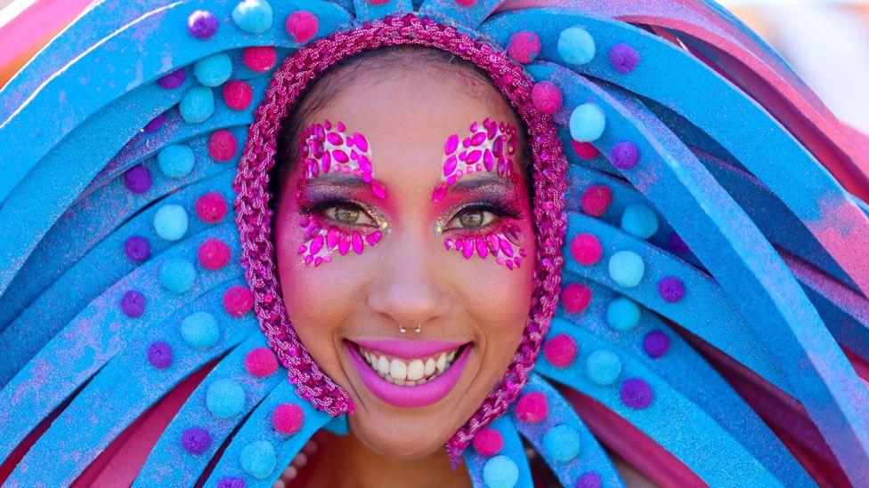 A female performer smiles in a pink and blue headdress - with pink sequins around her eyes and pink lipstick poses at a carnival in Cape Town ahead of the 2024 Earthshot Prize - Wednesday 6 November 2024