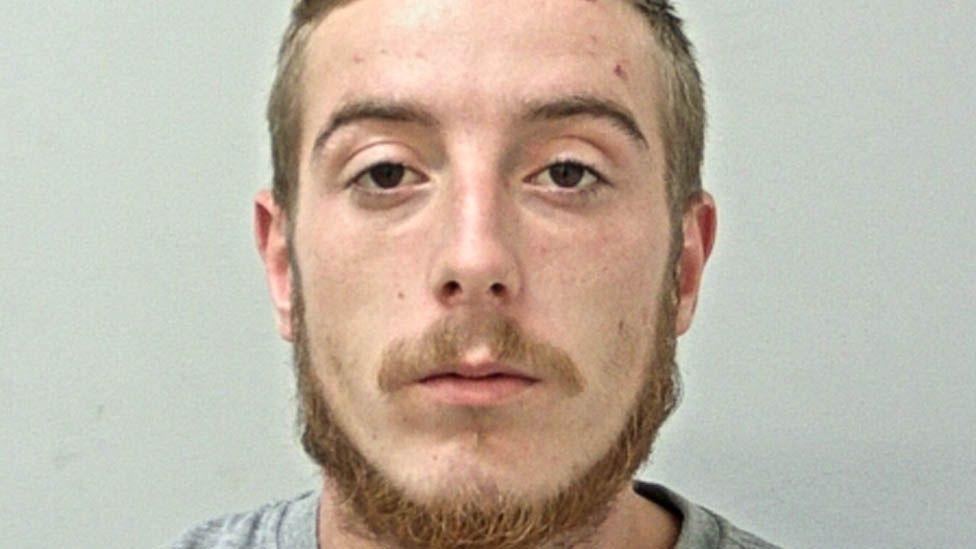 Jez Shepherd's mugshot. He has dark brown eyes, and mousey short hair, moustache and chin beard