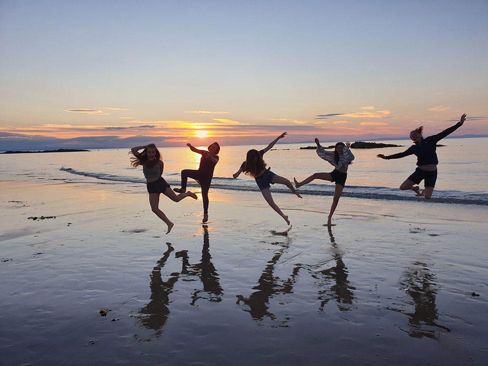 A group of people dance and jump on a beach as the sun sets