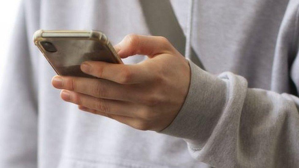 Teenage boy in grey hoodie holds phone