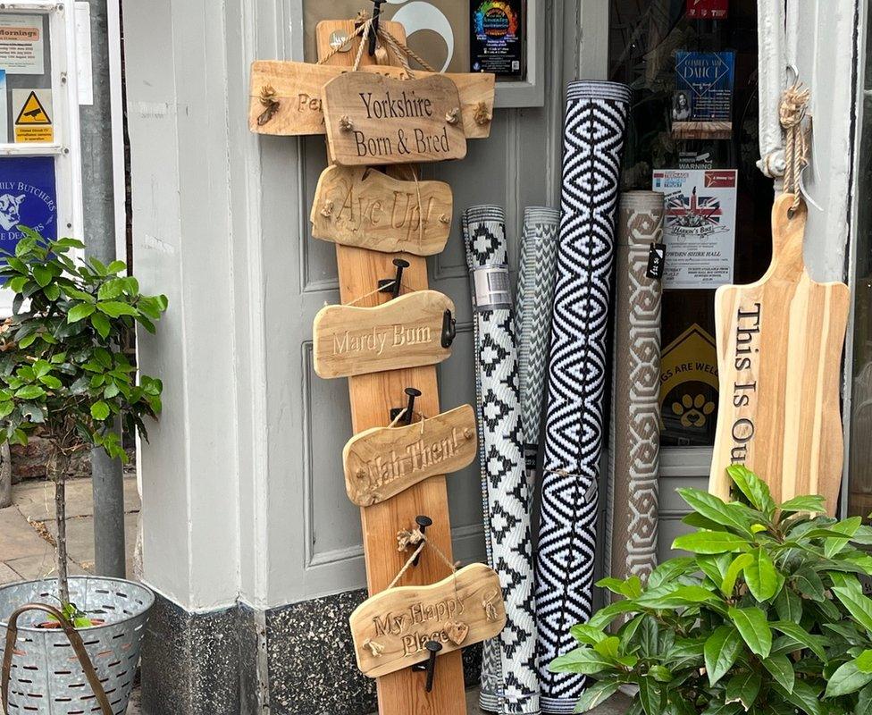 hand-carved, wooden signs outside a Howden shop. One reads "Mardy Bum". Another reads "My Happy Place"