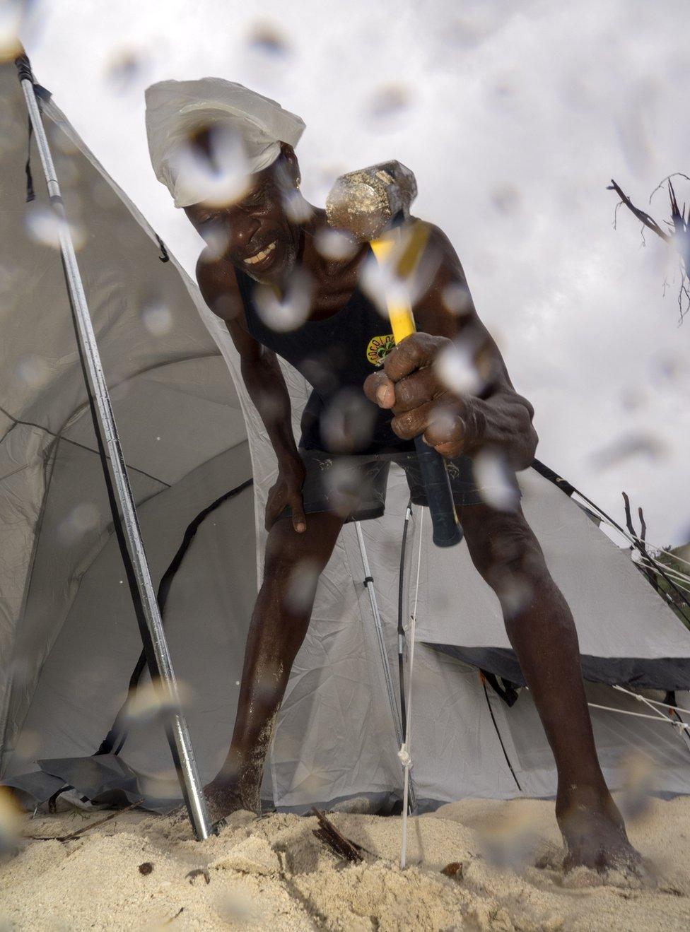 A man hammers a tent up amongst the rain