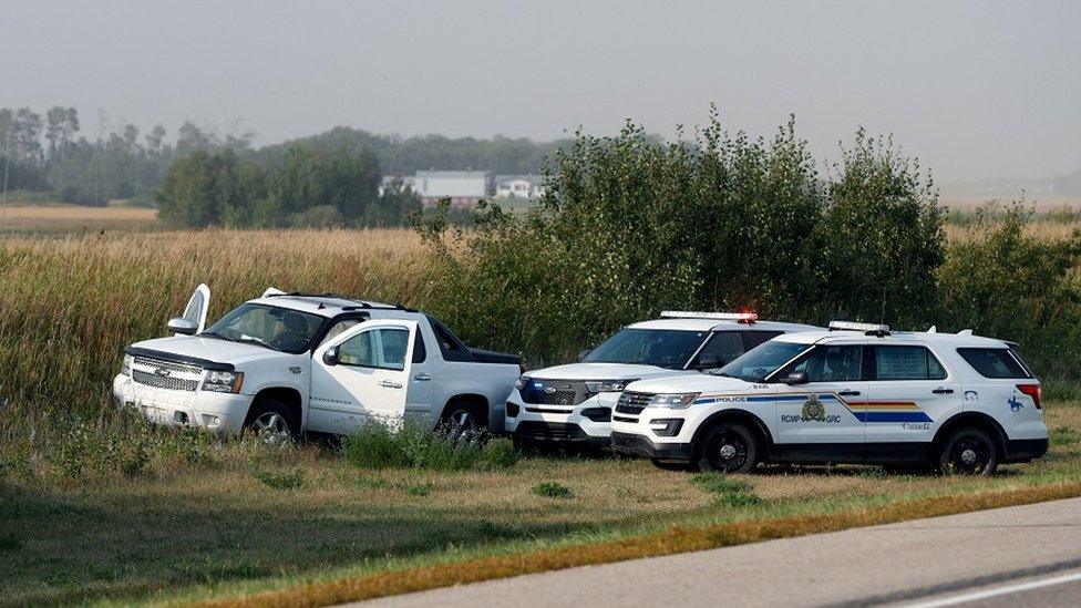 A Royal Canadian Mounted Police officer takes a pictures of police vehicles next to a pickup truck at the scene where suspect Myles Sanderson was arrested, along Highway 11 in Weldon, Saskatchewan, Canada, on September 7, 2022.