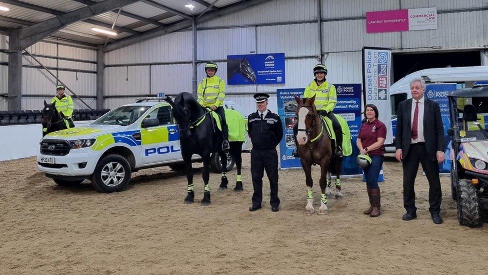 Volunteers on horseback wearing reflective clothes and standing next to a police car