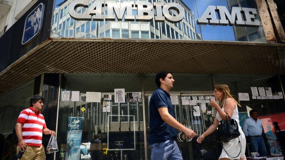 People walk past a closed bureau de change in downtown Buenos Aires on December 16, 2015. Argentina said Wednesday it will eliminate the foreign exchange restrictions that have propped up the official value of the peso since 2011, setting up a potentially painful devaluation. AFP